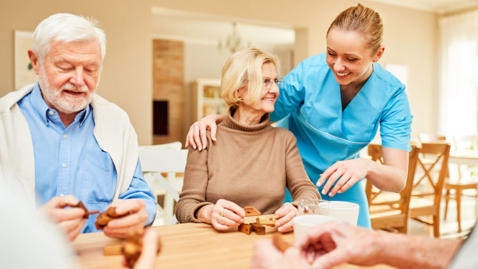 Caregiver smiling and playing game with older couple-Assisted living myths