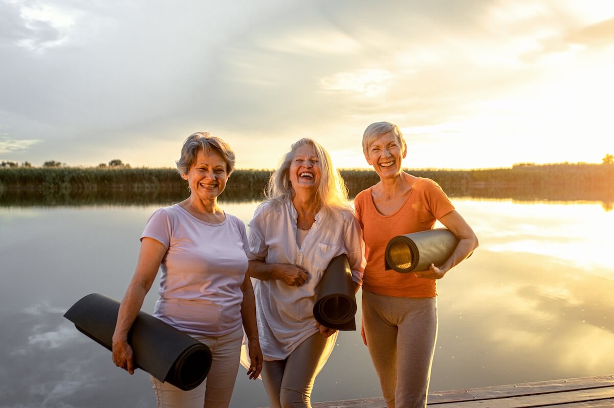 Portrait of three senior woman with yoga mats by the lake.
