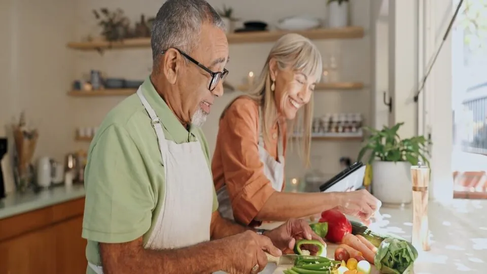 senior nutrition Kitchen, vegetables and elderly couple with cooking for healthy dinner, nutrition or bonding. Retirement, senior man and woman with ingredients at home for meal prep, support or happiness in marriage