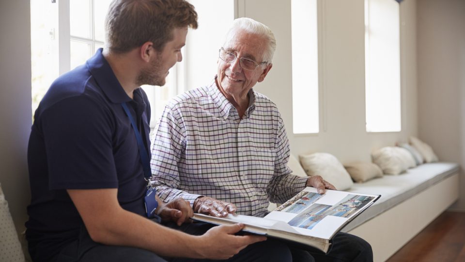 An elderly senior struggling with dementia looks through a photo album and talks with his son about the memories they shared in the past