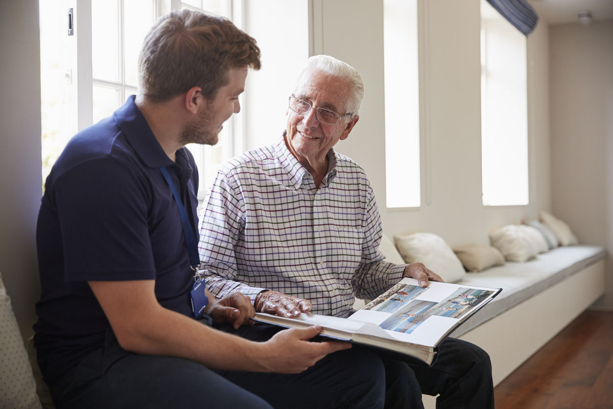 An elderly senior struggling with dementia looks through a photo album and talks with his son about the memories they shared in the past