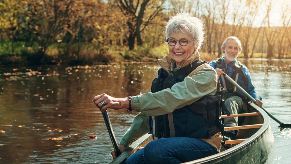 A senior couple smile as they kayak on Lake Guntersville, embracing the elements of nature to boost their mental health.